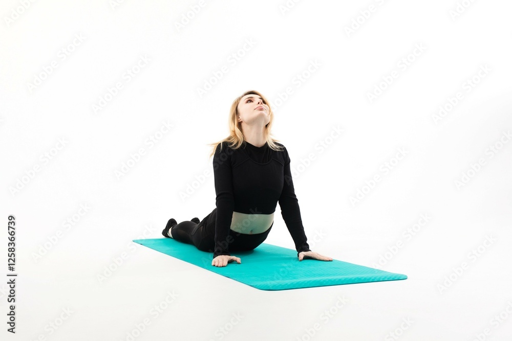 Fototapeta premium Woman practicing yoga in cobra pose on a teal mat in a bright indoor space
