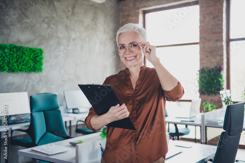 Photo of professional mature lady corporate leader touch specs hold documents wear brown shirt coworking nice light office photo