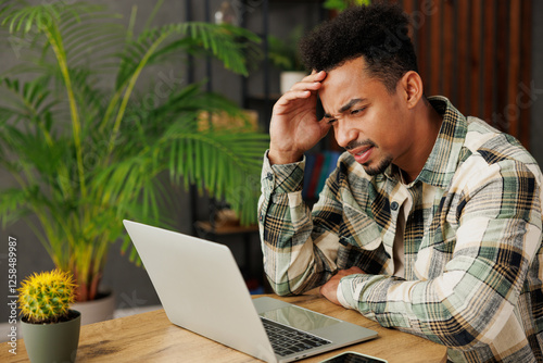 Young sad dissatisfied displeased IT man he wear grey casual clothes hold use work on laptop pc computer sitting alone at table in coffee shop cafe relax rest in restaurant during free time indoors. photo