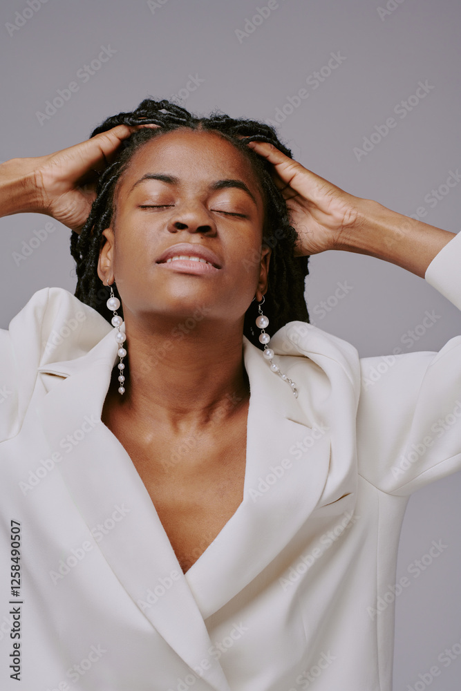 African American woman relaxing with eyes closed, wearing white clothing and earrings. She appears calm and peaceful while holding her hands behind her head African American woman relaxing with eyes closed, wearing white clothing and earrings. She appears calm and peaceful while holding her hands behind her head