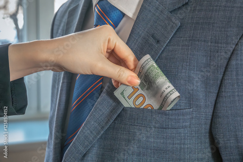 Hand puts dollar bills into the pocket of a man in a suit and tie standing opposite. To give a bribe. Corruption