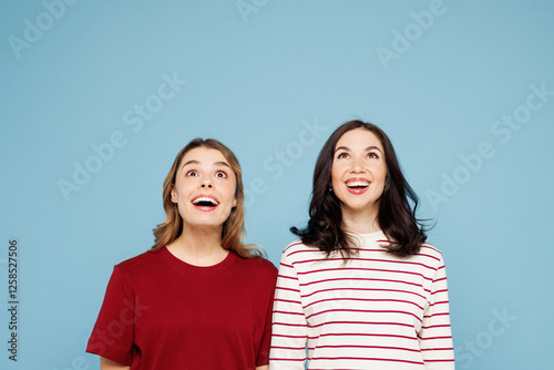 Young shocked surprised couple two friends women wear red casual clothes together look overhead on area mockup isolated on pastel plain light blue cyan background studio portrait. Lifestyle concept. photo