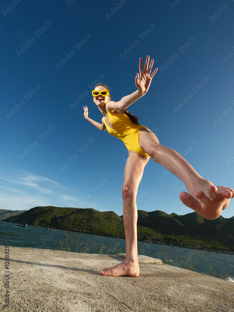 Yellow swimsuit woman standing on rocky edge near water and mountains in background, capturing a scenic and adventurous moment by a natural landscape Yellow swimsuit woman standing on rocky edge near water and mountains in background, capturing a scenic and adventurous moment by a natural landscape