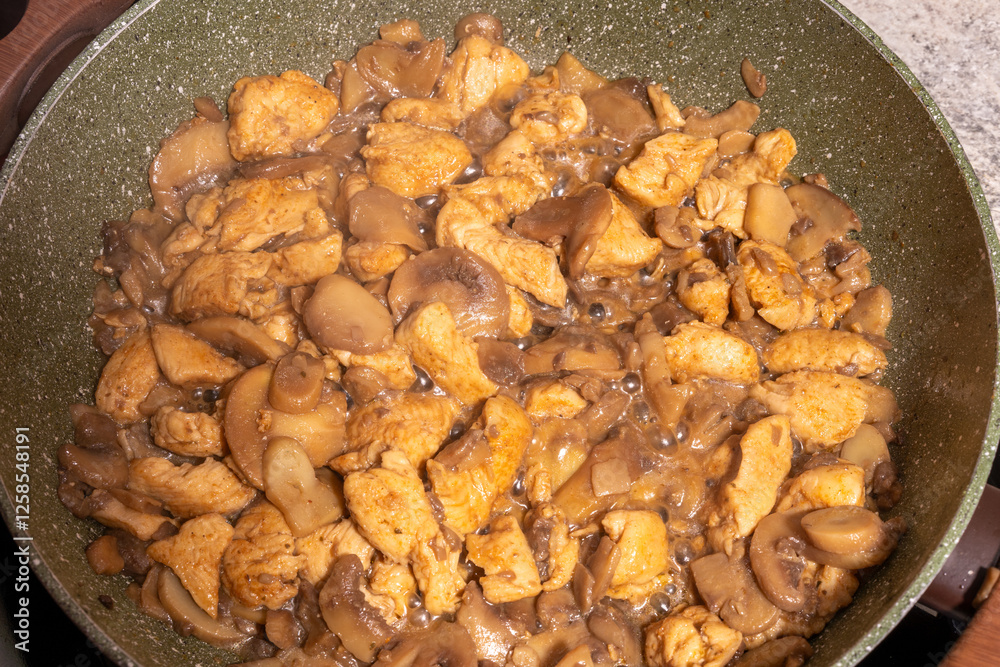 A close-up view of a pan filled with cooked chicken pieces and sliced mushrooms.