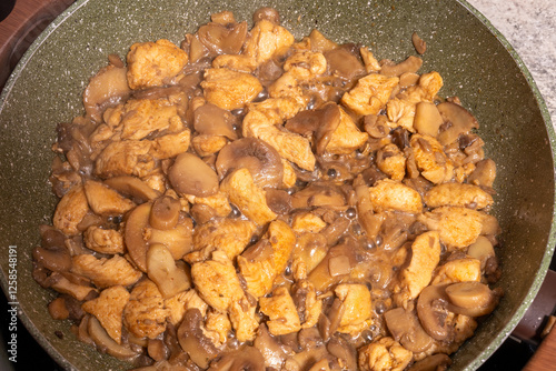 Obraz na płótnie A close-up view of a pan filled with cooked chicken pieces and sliced mushrooms. w salonie