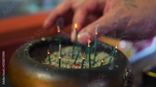 Burning incense sticks emit thin trails of smoke in a serene setting with a blurred red background, likely at the Byodo In Temple in Hawaii.