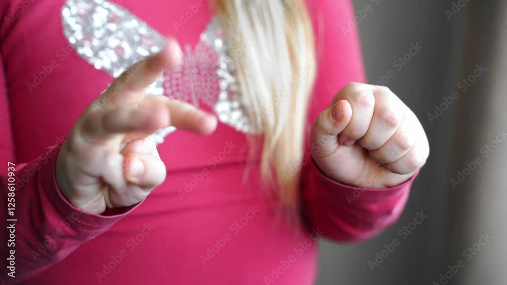 Girl extends hands forward, moves fingers. She spreads fingers wide, changes position. Palms face the camera. She wears pink long-sleeve shirt. Close-up of hand gestures and movement