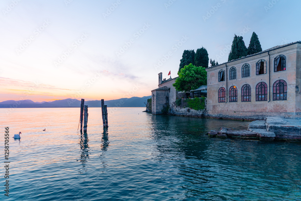 Swans on Garda Lake, Punta San Vigilio, Italy. Sunset view of historic building.