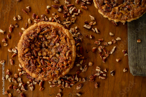 Tartaletas de nuez caramelizada sobre tabla de madera oscura con nueces picadas alrededor
