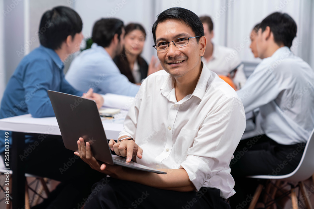 Confidence and happy smiling businessman portrait with background of his colleague and business team working in office. Office worker teamwork and positive workplace concept. Prudent Confidence and happy smiling businessman portrait with background of his colleague and business team working in office. Office worker teamwork and positive workplace concept. Prudent