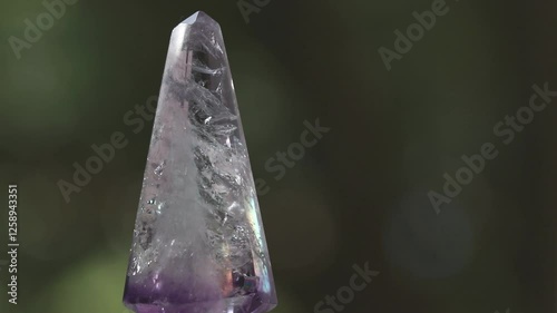 Rotating faceted amethyst crystal and dark background.