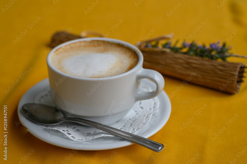 Warm coffee cup on a vibrant yellow tablecloth with a touch of nature beside it