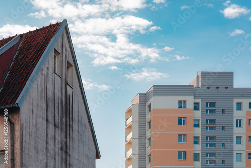 Old Gabled House with Red Tiled Roof Contrasting a Modern Pastel Apartment Building under a Bright Sky