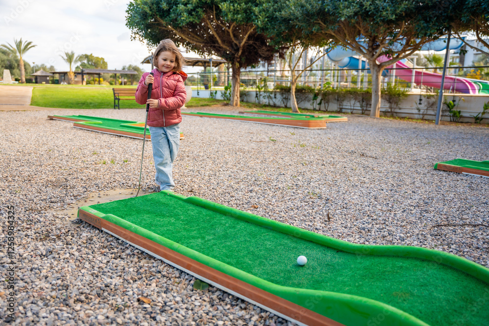 Fototapeta premium Little girl playing mini golf outdoor. Child having fun with new activity in spring time. Family vacations or resort.
