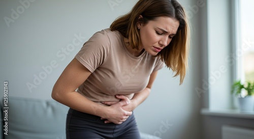 Young Woman Experiencing Abdominal Pain Holding Stomach Indoors by Window