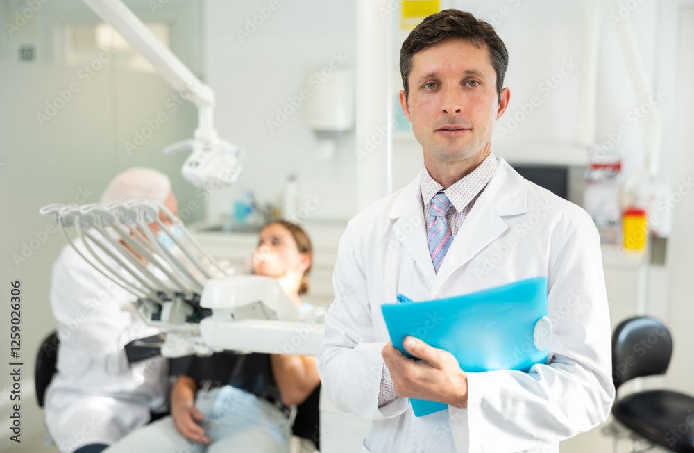 Fototapeta premium Adult male nurse taking notes while examining patient in dental office