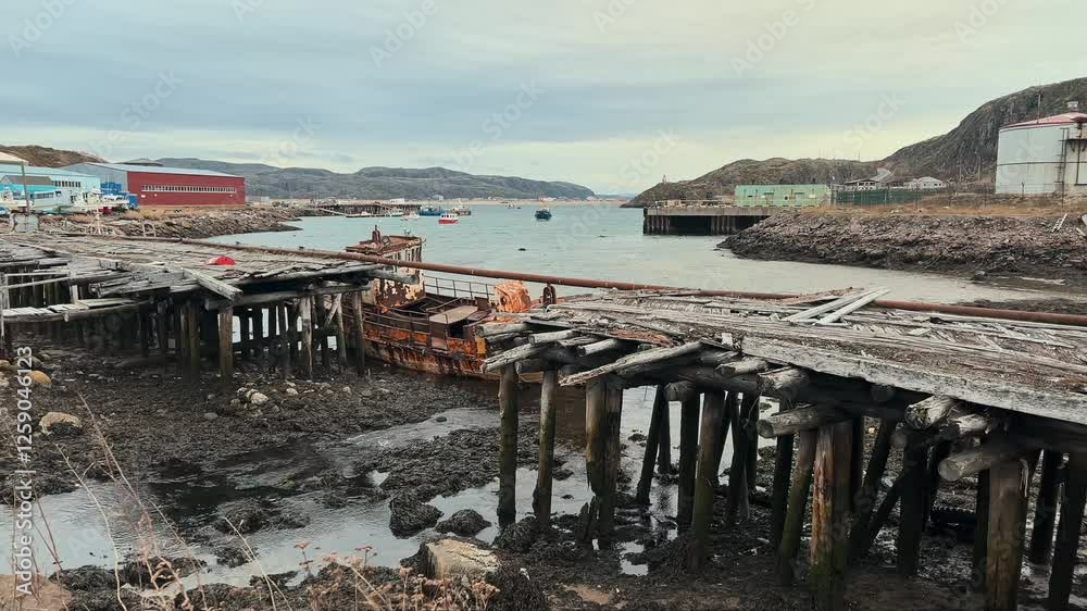 Old, abandoned wooden bridge in fishing port town was destroyed by flood from nearby river. rusted ship stranded next to bridge. Teriberka, Russia Old, abandoned wooden bridge in fishing port town was destroyed by flood from nearby river. rusted ship stranded next to bridge. Teriberka, Russia