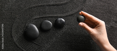 Photography Female hand and stones on black sand with lines. Zen concept