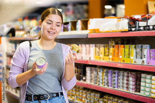 Caring interested young woman visiting pet store in search of tasty and healthy canned wet food for loved cat