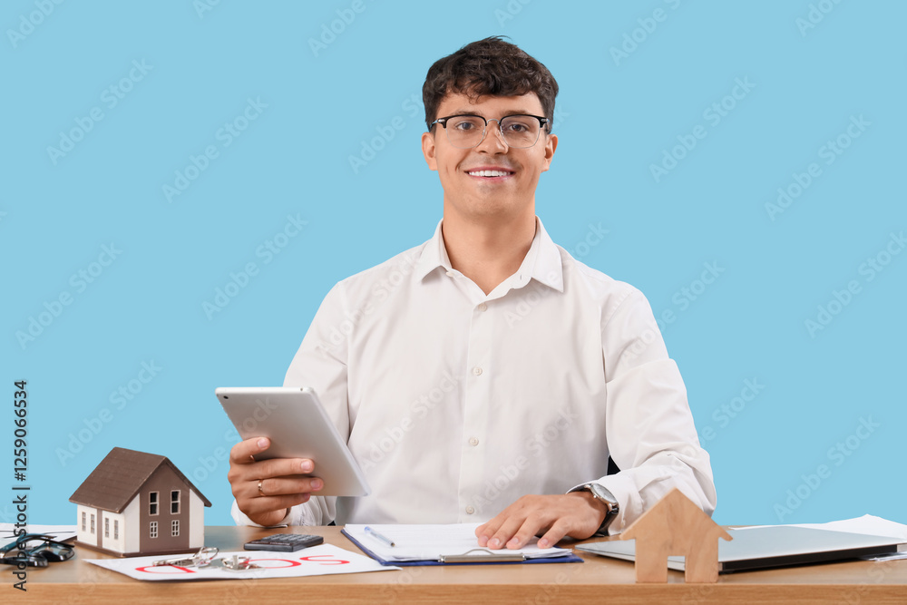 Male real estate agent working with tablet computer at table on blue background Male real estate agent working with tablet computer at table on blue background