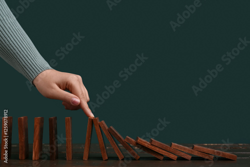 Fotografie Woman stopping domino effect at black wooden table
