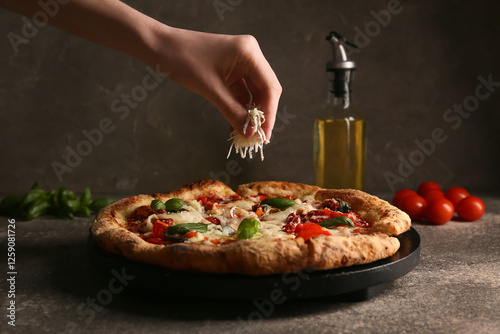 Hand adding grated cheese to tasty pizza Margarita on grunge background photo