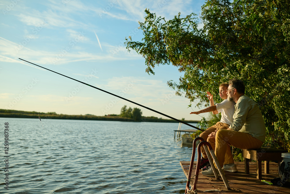 Grandfather and grandson enjoying a relaxing day fishing on a wooden dock Grandfather and grandson enjoying a relaxing day fishing on a wooden dock