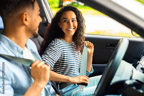 Excited millennial arab couple fastening seat belt, looking at each other and smiling, going vacation by car, side view, closeup. Mixed race young family having weekend trip, enjoying nice weather photo