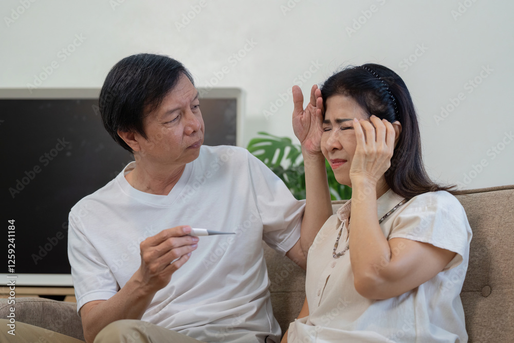 Elderly couple at home, one partner measuring temperature while the other has a headache. Elderly couple at home, one partner measuring temperature while the other has a headache.