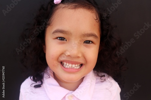 Closeup of Asian face, smiling toddler girl showing her healthy white teeth. photo