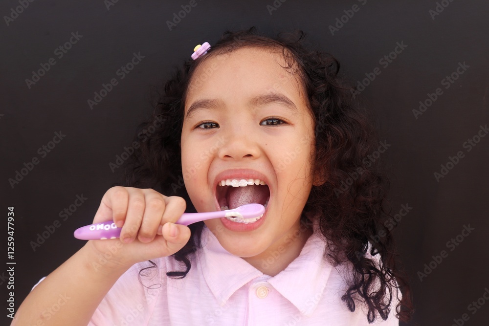 Closeup Asian Face, Toddler girl hand holding toothbrush she brushes her own teeth on black background,health medical care. Closeup Asian Face, Toddler girl hand holding toothbrush she brushes her own teeth on black background,health medical care.