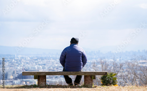 高台のベンチに座って街を眺める高齢の男性の後ろ姿