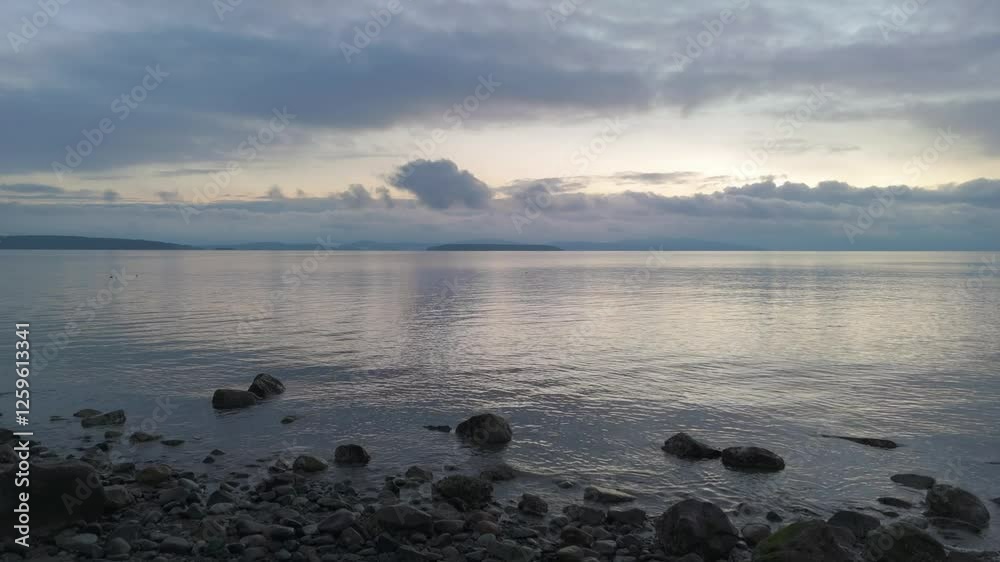 Calm ocean scene at dusk, cloudy sky reflecting on still water, rocky beach in the foreground, serene and tranquil nature video. British Columbia, Canada. Calm ocean scene at dusk, cloudy sky reflecting on still water, rocky beach in the foreground, serene and tranquil nature video. British Columbia, Canada.