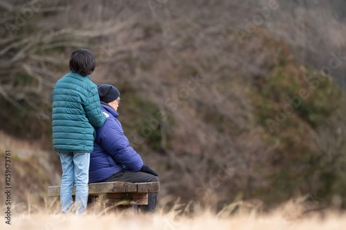 ベンチに座る高齢男性に寄り添う若者