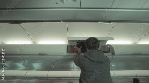 A passenger places their bag in the overhead compartment of an airplane. The photo captures the experience of traveling and navigating the cabin space.