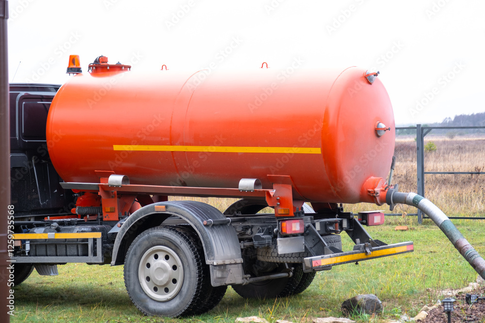 The orange tank of the sewage disposal machine in the courtyard of the house sucks sewage waste from the septic tank well. Waste disposal service, sewage disposal