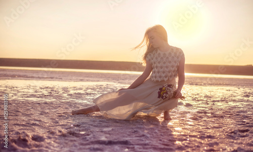 Blonde girl with a straw hat sits in the middle of a salt lake photo