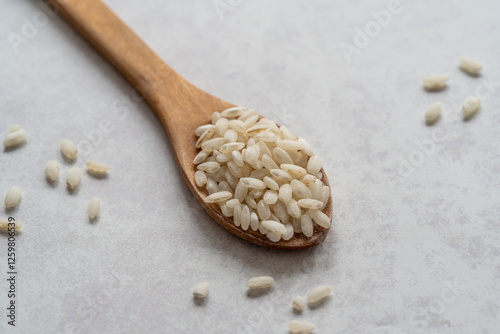 Arborio white rice in wooden spoon close up. Macro photo of white rice in wooden spoon on grey background. 