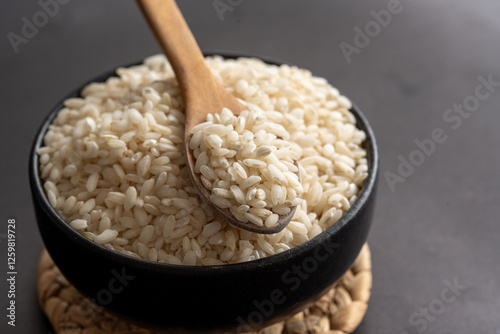 Macro photography of white short grain rice in wooden spoon on dark background. Short white rice in wooden spoon. Closeup photo of rice. 