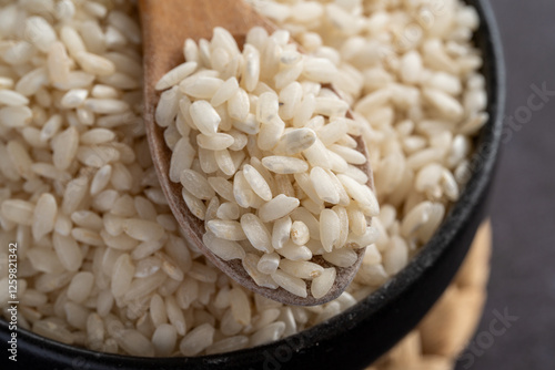 Macro photography of white short grain rice in wooden spoon on dark background. Short white rice in wooden spoon. Closeup photo of rice. 