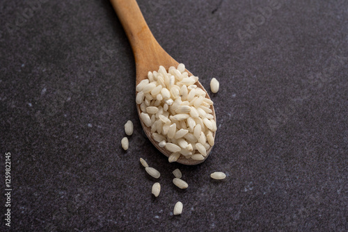 White short grain rice in wooden spoon on dark background. White rice on dark background