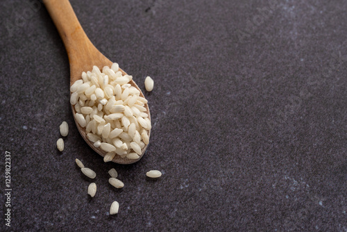 White short grain rice in wooden spoon on dark background. White rice on dark background