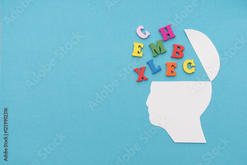 Silhouette of an open human head with colorful letters spilling out on blue background, concept of learning and dyslexia