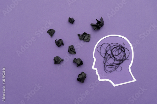Outline of a Human Head with black tangled thread and crumpled paper on purple background, concept of stress and mental overload