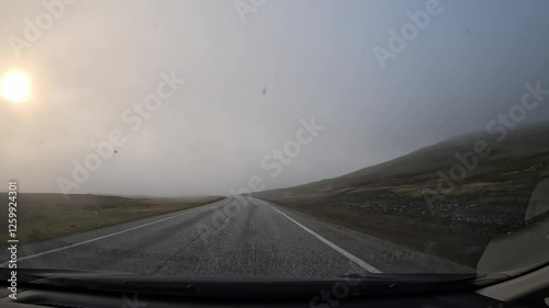 Driving on the E69 road through the tundra in northern Norway. Misty hills covered with grass and scattered stones surround the route, creating a remote and atmospheric landscape. photo