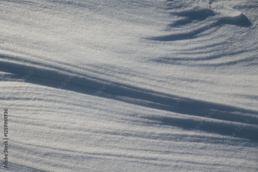 dettagli della superficie di un terreno naturale coperto dalla neve con forme variabili disegnate dal vento ed illuminate dal sole, di giorno, in inverno