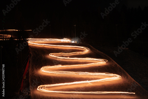 Obraz na płótnie scia luminosa disegnata dalle luci di file di sciatori che scendono lungo una pista innevata di notte w salonie