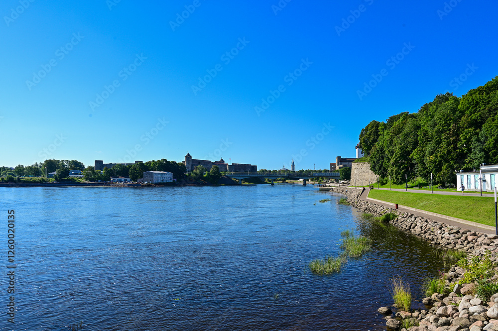 Obraz premium View from Narva in Estonia over the border river Narva and the Russian border to the Ivangorod Fortress in Ivangorod in Russia in summer under a blue sky