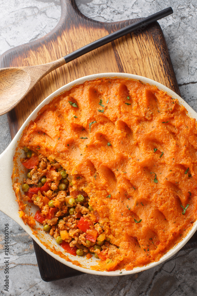 Healthy shepherd's pie made with ground meat, vegetables and topped with a layer of fluffy mashed sweet potatoes closeup on the baking dish on the wooden board. Vertical top view from above