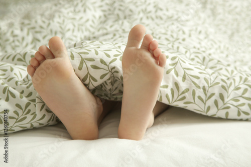 Child feet under the green and white duvet